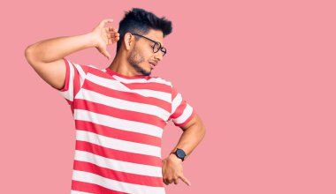 Yakışıklı Latin Amerikalı genç adam, gündelik kıyafetler ve gözlük takıyor, geriniyor, yorgun ve rahat, uykulu ve sabahın erken saatlerinde esniyor. 