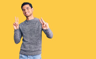 Latin asıllı yakışıklı süveter giyen genç adam kameraya bakıp zafer işareti yapıyor. İki numara.. 