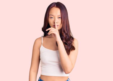 Gündelik giysiler giyen genç, güzel Çinli bir kız parmakları dudaklarında sessiz olmak istiyor. sessizlik ve gizli konsept. 