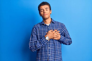 Sıradan kıyafetler giyen, göğsünde elleri kapalı, yüzünde minnet dolu jestlerle gülümseyen Afrikalı genç bir Amerikalı. sağlık kavramı. 