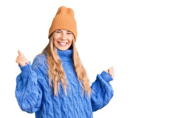 Sarı saçlı, yün kazak giyen, kışlık şapkalı güzel beyaz kadın kolları havada, gülümseyen ve başarı çığlıkları atan mutlu ve heyecanlı bir jest yapıyor. kutlama konsepti. 