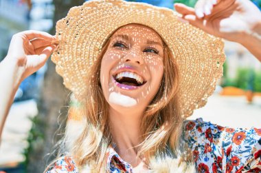 Yaz şapkası takmış, mutlu bir şekilde gülümseyen güzel sarışın bir kadın. Şehrin caddesinde yüzünde gülümsemeyle dikilirken.
