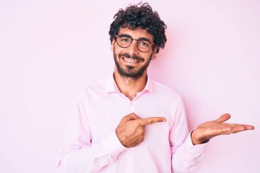 Kıvırcık saçlı ve ayı gibi iş gömleği ve gözlüklü yakışıklı genç adam kameraya hayret ediyor ve gülümsüyor.. 