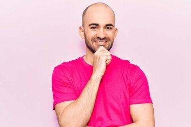 Genç, kel, sıradan bir tişört giyen, kolları çapraz ve çenesi açık kameraya gülümseyen yakışıklı bir adam. Olumlu düşünmek. 