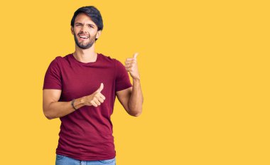 Yakışıklı İspanyol bir adam, günlük giysiler içinde. Arka tarafı işaret ediyor. El ve baş parmakları havada, kendinden emin. 