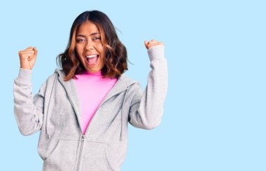 Genç, güzel, melez ve sportif giysiler giymiş bir kadın. Başarının şaşkınlığını ve şaşkınlığını kolları açık ve gözleri açık bir şekilde kutluyor. Kazanan konsept. 