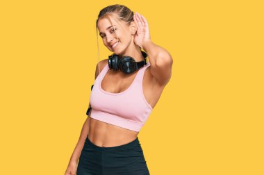 Spor kıyafetleri giyen, kulaklık takan, ağzı kulaklarında gülümseyen, dedikoduları ve dedikoduları dinleyen genç sarışın bir kadın. Sağırlık kavramı. 