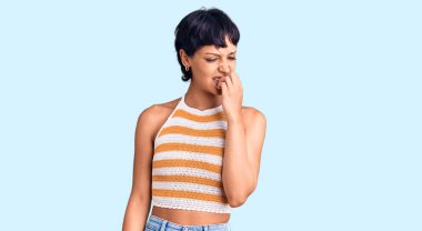 Kısa saçlı, sıradan kıyafetler giyen genç esmer kadın elleri ağızda, tırnaklarını yiyormuş gibi gergin ve stresli görünüyor. anksiyete. 