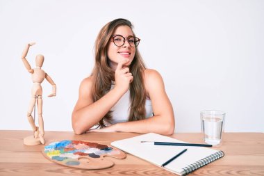 Masada oturan güzel beyaz kadın ressam kameraya kollarını kavuşturmuş ve çenesi üzerinde kendinden emin bir şekilde bakıyor. Olumlu düşünmek. 