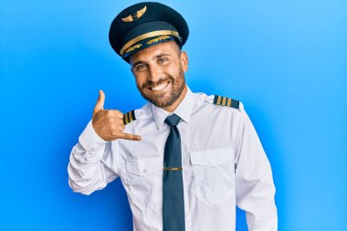 Sakallı, uçak pilotu üniforması giyen, gülümseyen, el ve parmaklarıyla telefonla konuşan yakışıklı bir adam. iletişim kavramları. 