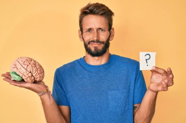 Beyni sakallı ve soru işareti olan, kafası karışık, yakışıklı beyaz bir adam. şüphe kavramı. 