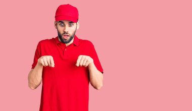 Sakallı, teslimat üniformalı genç yakışıklı bir adam parmaklarını göstererek reklamını yapıyor, şaşırmış bir yüz ve açık bir ağız. 