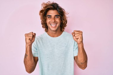 Gündelik giysiler giyen genç İspanyol adam şaşkınlık ve şaşkınlık içinde kollarını kaldırarak ve gözlerini açarak başarıyı kutluyor. Kazanan konsept. 