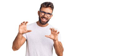 Günlük kıyafetler ve gözlük takan genç İspanyol adam komik bir şekilde gülüyor kedi gibi pençe hareketi yapıyor, agresif ve seksi bir ifade. 