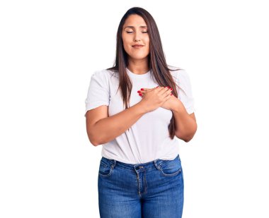 Genç, güzel, esmer, sıradan tişörtler giyen, elleri göğsünde, gözleri kapalı ve yüzünde minnet ifadesi olan bir kadın. sağlık kavramı. 