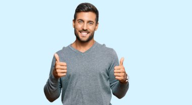 Yakışıklı İspanyol bir adam günlük kıyafetler giyiyor. Başarı işareti yapıyor. Elleriyle olumlu jest yapıyor. Neşeli ifade ve kazanan jest. 