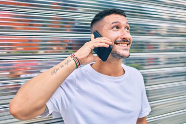 Genç İspanyol adam gülümsüyor. Akıllı telefonda konuşuyor. Duvara yaslanıyor.