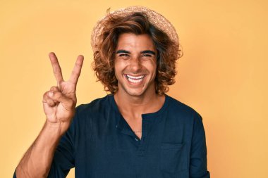 Yaz şapkası takan genç İspanyol adam iki numarayı gösterip işaret ederken kendinden emin ve mutlu gülümsüyor.. 