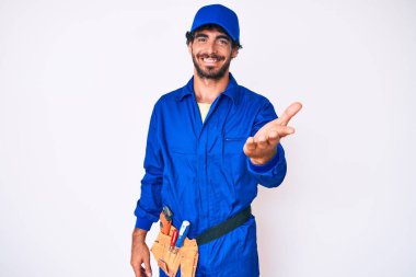 Kıvırcık saçlı yakışıklı genç adam ve ayı gibi giyinen tamirci üniforması. Gülümseyen neşeli avuç içi yardım ve kabullenme eli.. 