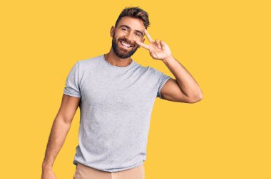 Gündelik kıyafetler giyen genç İspanyol adam barış sembolü yapıyor. Yüzünde parmaklar, gülümseyerek zaferi gösteriyor. 