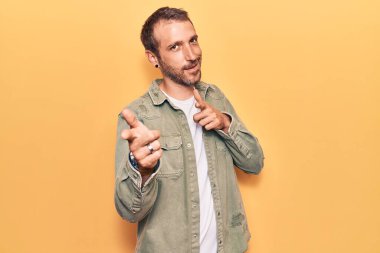 Gündelik giysiler giymiş genç yakışıklı adam mutlu ve komik yüzüyle kamerayı işaret ediyor. iyi enerji ve titreşimler. 
