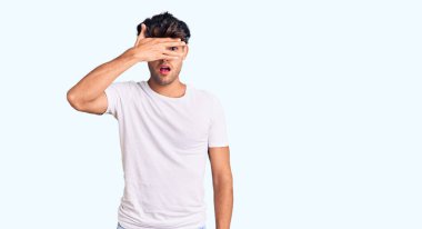 Gündelik kıyafetler giyen genç İspanyol adam şok içinde yüzünü ve gözlerini kapayarak utanmış ifadesiyle parmaklarından bakıyor.. 