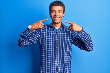 Gündelik kıyafetler giyen, neşeli gülümseyen, parmaklarıyla ve ağzıyla işaret eden Afrikalı genç bir Amerikalı. diş sağlığı kavramı. 
