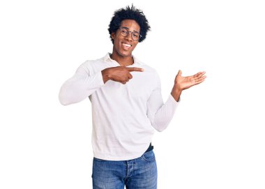 Afro saçlı, sıradan giyinmiş ve gözlüklü yakışıklı Afro-Amerikalı adam kameraya hayret ediyor ve gülümsüyor.. 