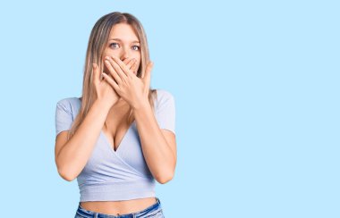 Gündelik giysiler giyen genç, güzel sarışın kadın yanlışlıkla elleri ile ağzını kapatırken şok oldu. gizli kavram. 