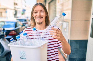 Sarışın, uzun saçlı ve sakallı beyaz bir adam plastik şişeleri geri dönüştürüyor.