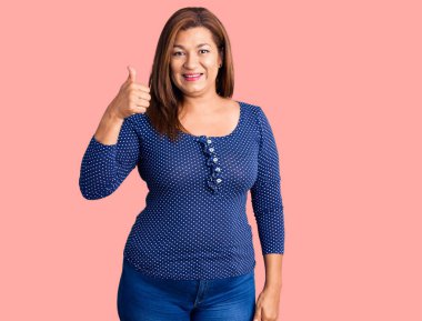 Orta yaşlı, sıradan kıyafetler giyen, mutlu ve pozitif gülümseyen, mükemmel ve onay işareti yapan Latin bir kadın. 