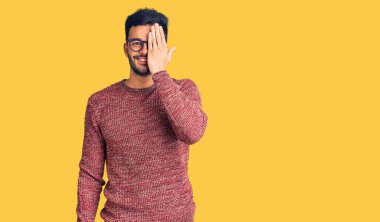 Genç, yakışıklı, süveter giyen ve gözlüklü bir adam bir gözünü eliyle kapatıyor, yüzünde kendine güvenen bir gülümseme ve sürpriz bir duygu var.. 