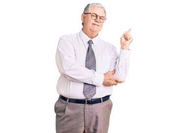 Yaşlı, gri saçlı, iş kıyafetleri giyen, yüzünde kocaman bir gülümseme olan, eli ve parmağı kameraya bakan bir adam.. 