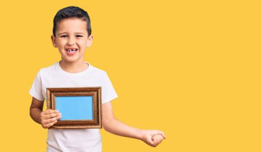 Küçük şirin çocuk boş bir çerçeve tutuyor gururla bağırıyor, zaferi kutluyor ve kollarını kaldırarak başarıyı kutluyor. 