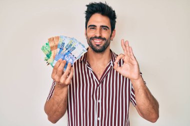 Sakallı yakışıklı İspanyol adam Güney Afrika rand banknotları tutuyor. Parmaklarıyla imza atıyor, gülümsüyor. 