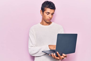 Genç Afrikalı Amerikalı bir adam dizüstü bilgisayar tutuyor. Düşünme tarzı ve ayık ifadesi. Kendine güveniyor gibi görünüyor. 