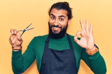 Genç Arap adam berber önlüğü takıyor. Parmaklarıyla imza atıyor. Gülümsüyor. 