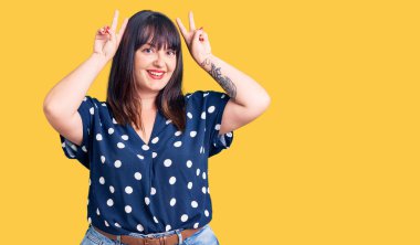 Genç ve cüsseli bir kadın komik ve çılgın poz veriyor parmakları tavşan kulağı gibi, neşeli gülümsüyor. 