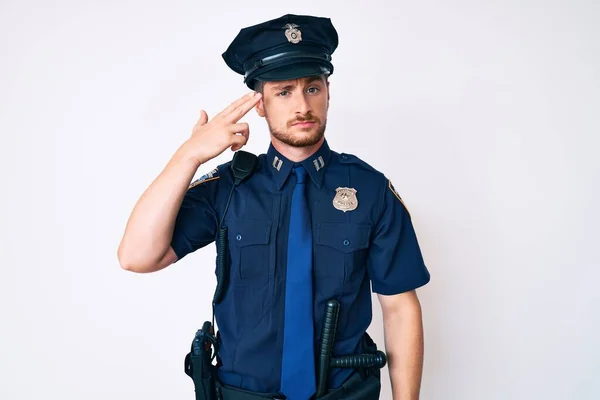 Young caucasian man wearing police uniform shooting and killing oneself pointing hand and fingers to head like gun, suicide gesture.