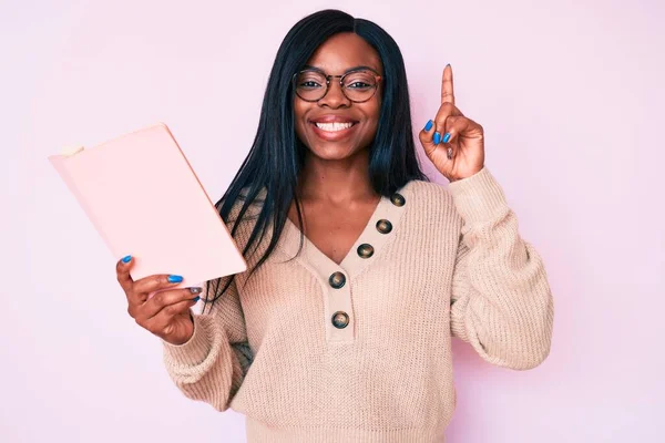 Młoda Afroamerykanka Okularach Książką Zaskoczona Pomysłem Lub Pytaniem Wskazującym Palcem — Zdjęcie stockowe