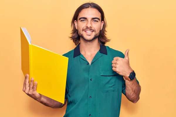 Joven Hombre Guapo Sosteniendo Libro Sonriendo Feliz Positivo Pulgar Hacia —  Fotos de Stock