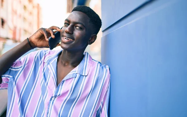 年轻的非洲裔美国人高兴地微笑着 坐在城市街道上的智能手机上 — 图库照片