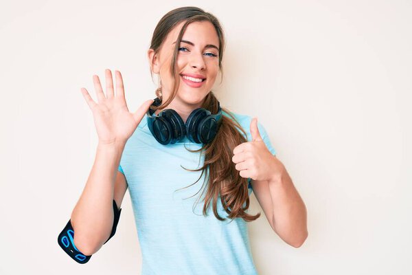Beautiful young caucasian woman wearing gym clothes and using headphones showing and pointing up with fingers number six while smiling confident and happy. 