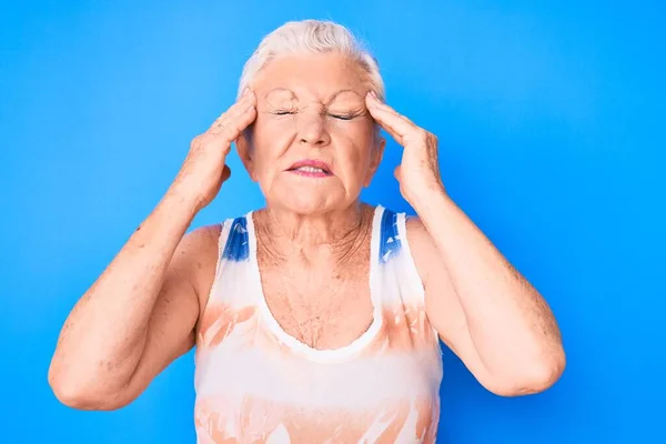 青い目と灰色の髪を頭の上に手でスポーティーなノースリーブシャツを着てシニア美しい女性は ストレスのために頭痛 片頭痛 — ストック写真