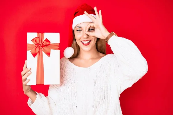 Молода Брюнетка Різдвяному Капелюсі Тримає Подарунок Усміхнений Щасливий Робить Знак — стокове фото