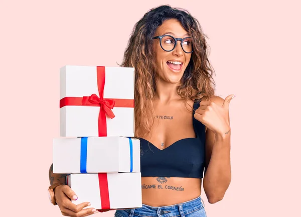 Young Hispanic Woman Tattoo Holding Gifts Pointing Thumb Side Smiling — Stock Photo, Image