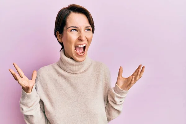 短い髪をした若いブルネットの女性は カジュアルな冬のセーターを着て狂気と怒りの叫びと積極的な表現と腕を上げて叫びました フラストレーションコンセプト — ストック写真