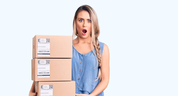 Young Beautiful Blonde Woman Holding Delivery Boxes Scared Amazed Open — Stock Photo, Image