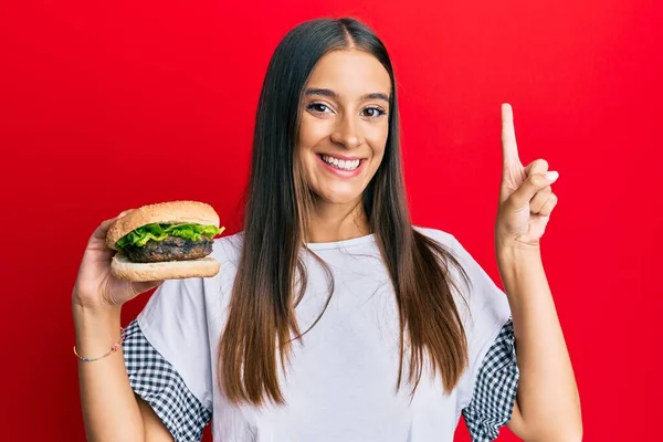 Young Hispanic Woman Eating Hamburger Surprised Idea Question Pointing Finger — Stock Photo, Image