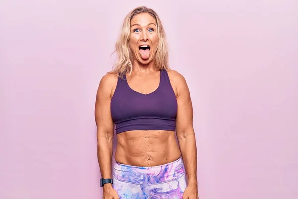 ピンクの背景にスポーツウェアを着た中年の白人ブロンド女性が面白い表情で幸せ舌を突き出しています 感情の概念 — ストック写真